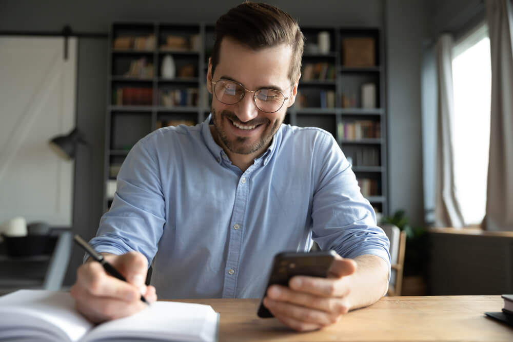 Smiling Businessman Wearing Glasses Using Phone Writing Important Information In