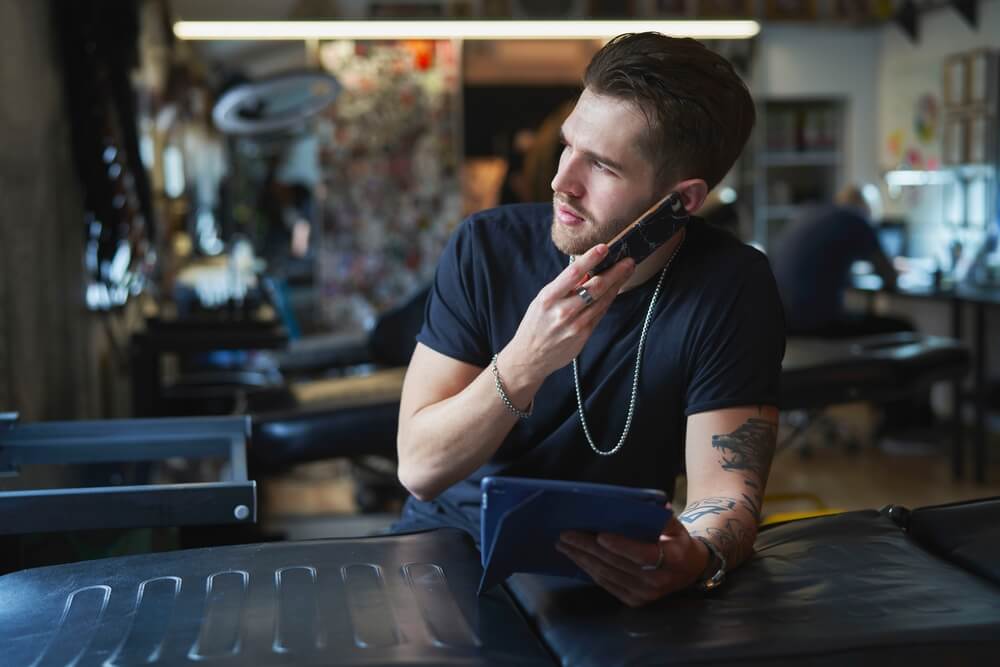 Caucasian tattoo artist talking by mobile phone and in tattoo